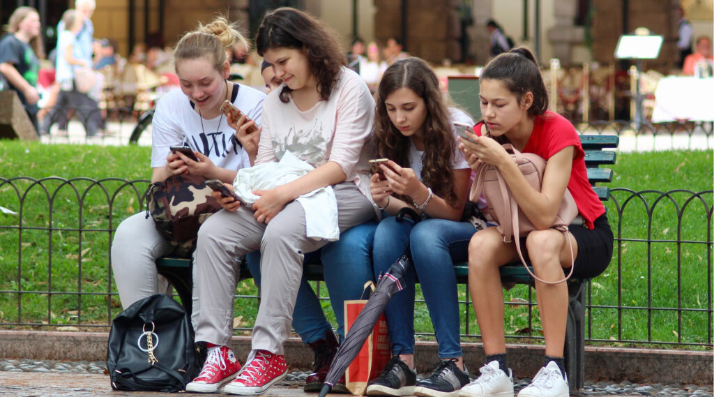 4 Mädchen auf Parkbank mit Smartphones